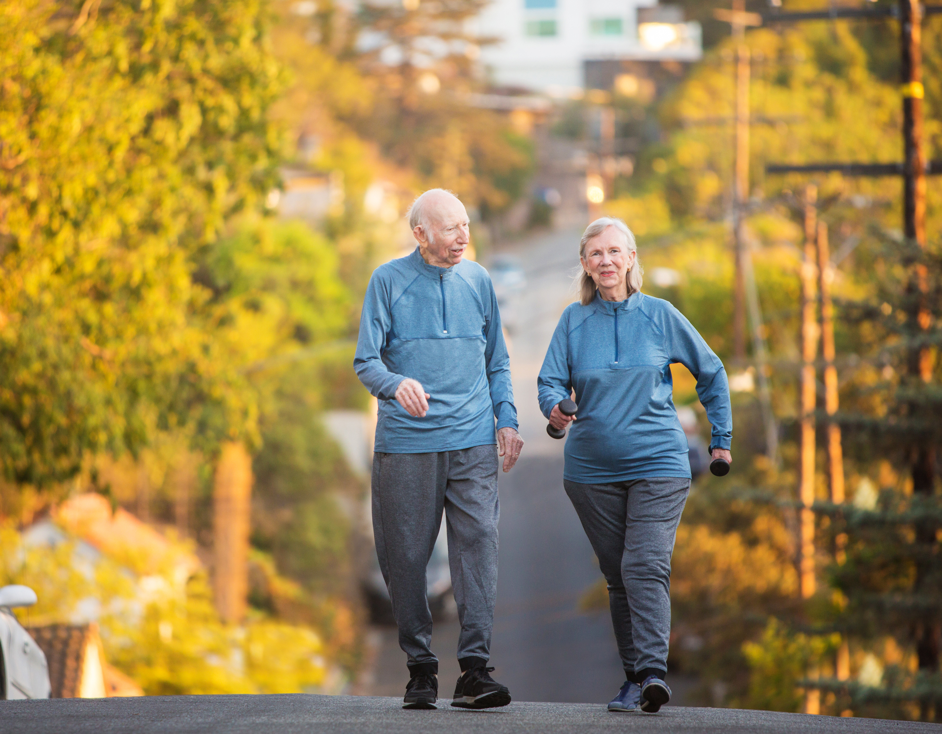 Two older adults walking together at sunset on a quiet residential street, exercising as part of a home-based program.